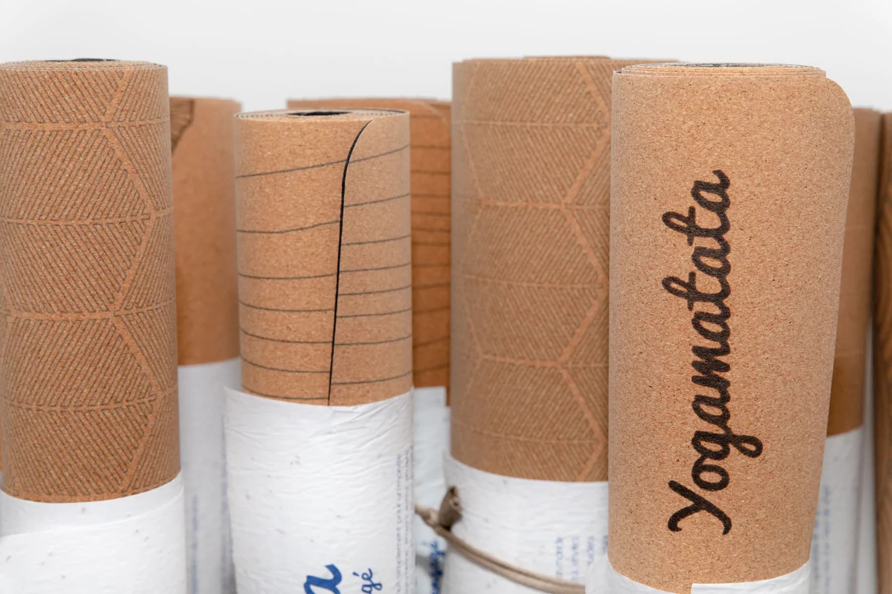 Des tapis de yoga en liège roulés côte à côte dans leurs bandes de papier, l'un marqué Yogamatata