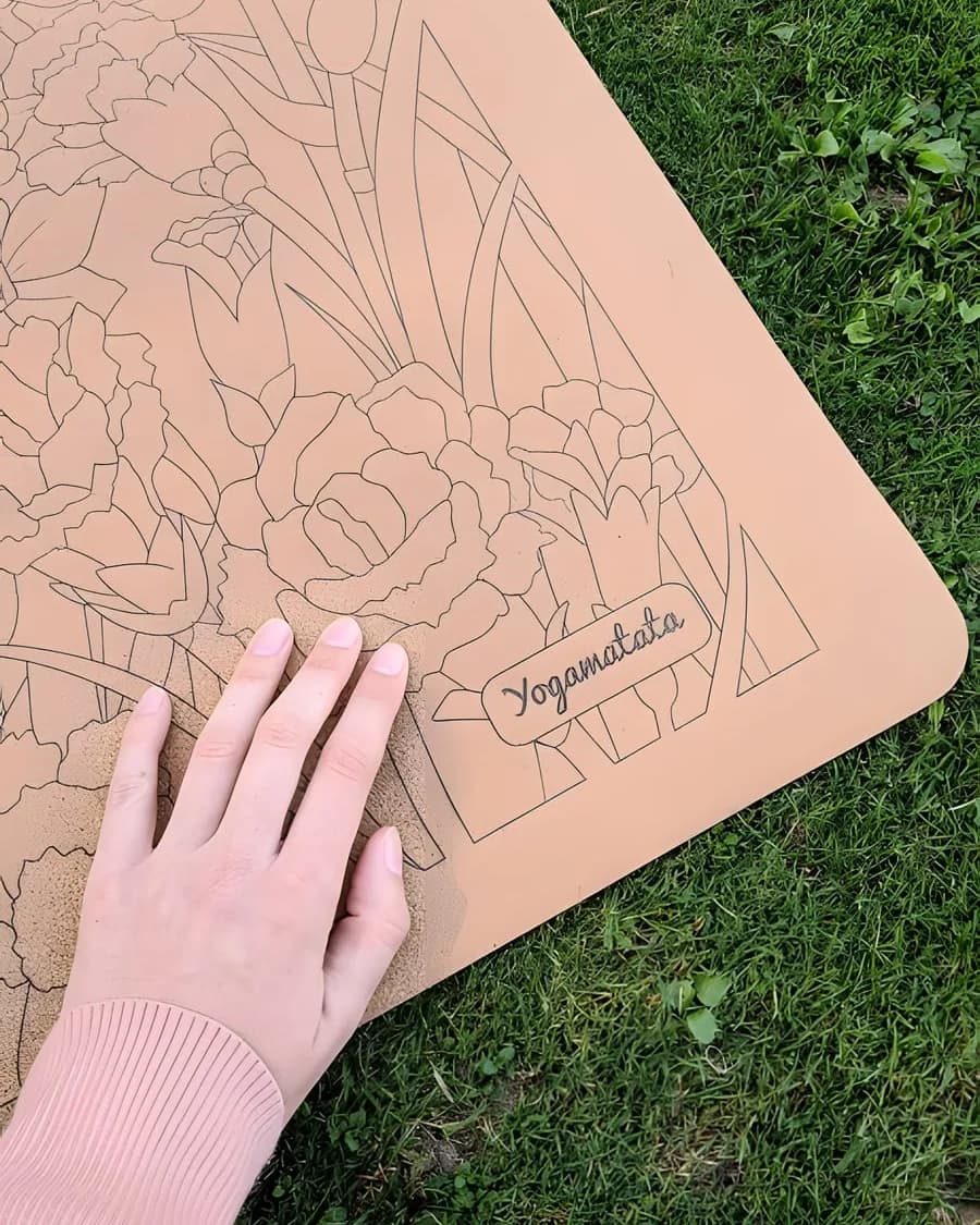 Une main posée sur un tapis en liège à motif floral, étendu dans l'herbe