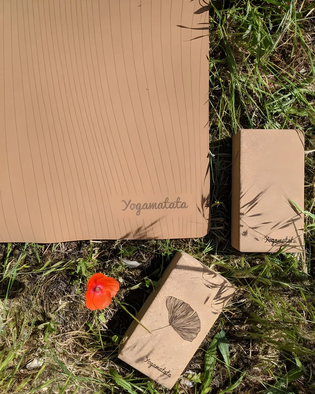 Un tapis Lignes et deux briques en liège posés dans l'herbe haute, à côté d'un coquelicot
